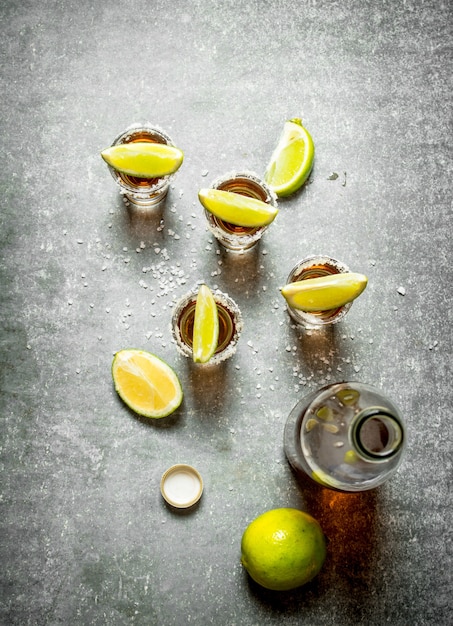 Bouteille de tequila avec de la chaux et du sel sur table en pierre.