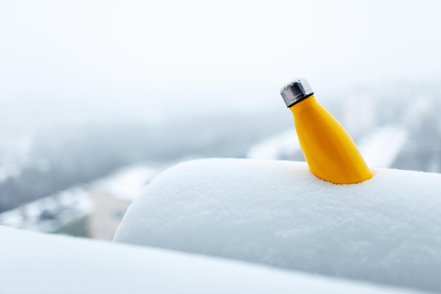 Bouteille thermo en acier de couleur jaune dans la neige Vue rapprochée Thermos réutilisable