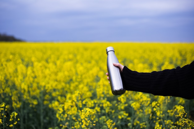 Bouteille thermos inox à la main, sur la surface du champ de colza.