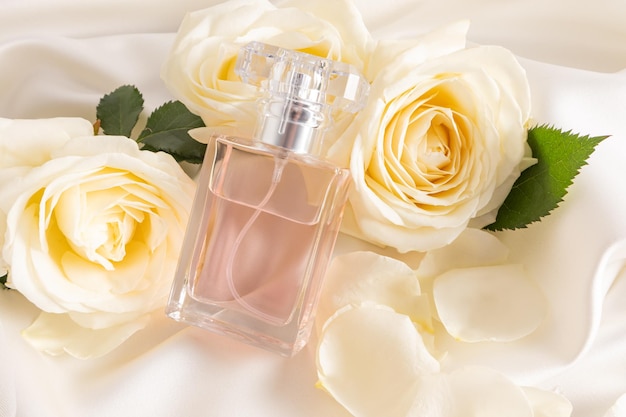 Une bouteille transparente avec un élégant parfum floral s'appuie sur des roses de thé blanches chics Présentation du parfum une bouteille sans nom pour la marque