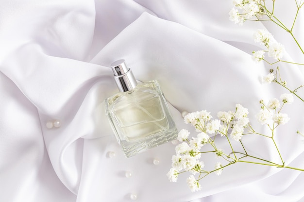 Une bouteille transparente de produit cosmétique repose sur un tissu texturé en satin blanc et de délicates fleurs de gypsophile un modèle pour le parfum