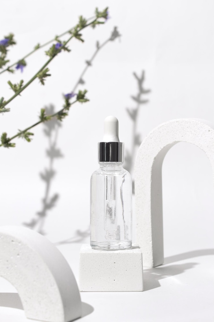 Bouteille transparente avec sérum de beauté acide hyaluronique en arche avec des fleurs de chicorée Cosmétique de soins de la peau Concept de beauté pour les soins du visage et du corps