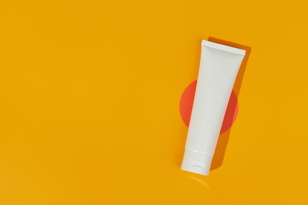 Bouteille de tube blanc vierge vue de dessus à plat avec crème de lotion ou nettoyant sur fond orange