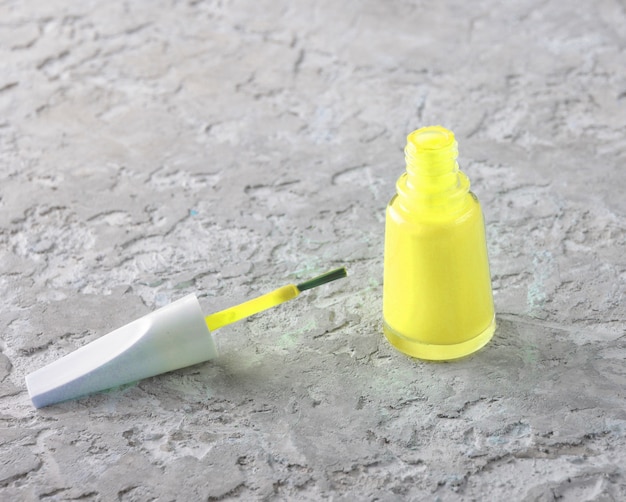 Une bouteille de vernis à ongles sur un béton gris.