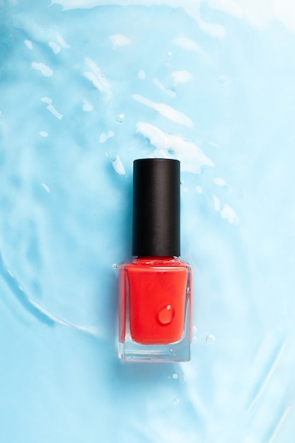 Bouteille de vernis à ongles de couleur rouge sur l'eau bleue, gros plan. Vue de dessus.