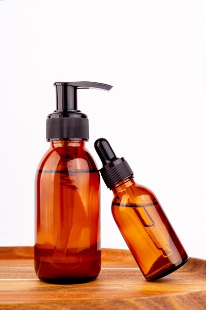 Photo bouteille de verre ambre foncé sérum plaque en bois soin naturel de la peau spa conception de produits de beauté huile organique minérale cosmétiques sur fond blanc mockup pipette huileuse traitement du visage et du corps layxa plat