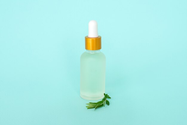 Bouteille en verre cosmétique avec de l'huile. contenant pour un produit pour femme avec de petites fleurs blanches sur fond turquoise. Pot cosmétique. Place pour le texte