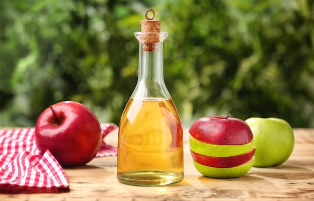 Bouteille en verre avec du vinaigre de pomme et des fruits frais sur une table en bois