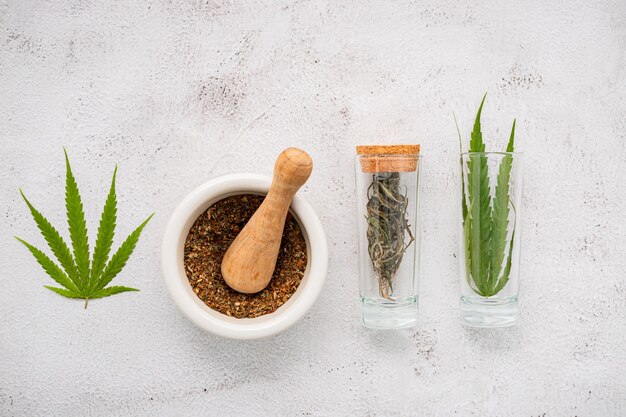 Bouteille en verre d'huile de cannabis avec du mortier blanc et des feuilles de chanvre posées sur du béton.