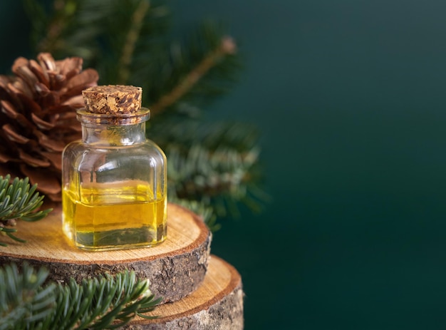 Bouteille en verre avec de l'huile essentielle de conifère près des branches de sapin et des pommes de pin sur le vert en gros plan