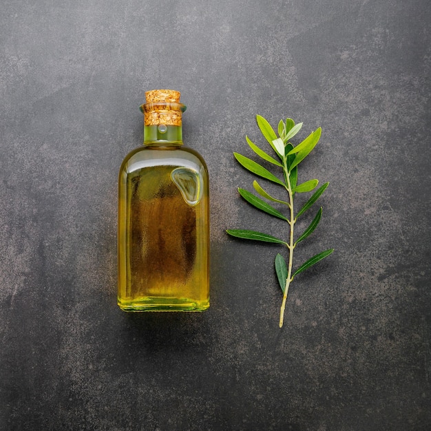 Bouteille en verre d'huile d'olive et branche d'olivier sur fond de béton foncé.