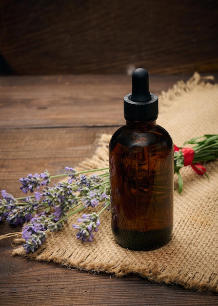 Une bouteille en verre marron avec une pipette et un bouquet de lavande sur une table en bois marron