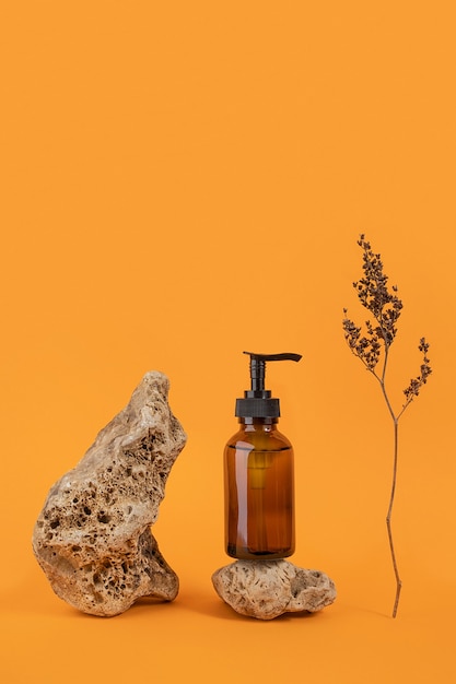 Bouteille en verre marron avec produit cosmétique sur pierre et fleurs séchées sur fond orange. Concept cosmétique de Spa bio naturel Vue de face.