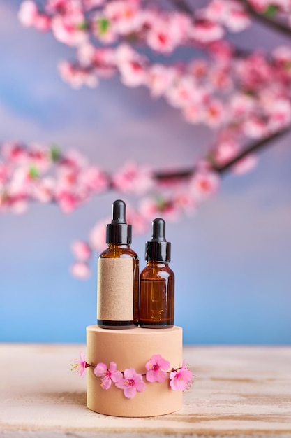 Bouteille en verre avec pipette et sérum sur un podium et des branches de cerises en fleurs