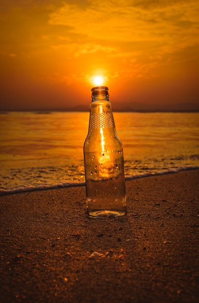Bouteille en verre sur le sable au coucher du soleil