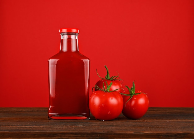 Bouteille en verre de sauce ketchup et tomates rouges fraîches sur table