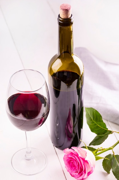 Bouteille en verre de vin avec bouchons et rose sur table en bois blanc
