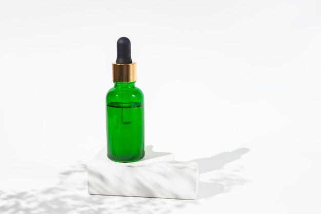 Bouteille verte avec de l'huile de cannabis utilisée à des fins médicales Fond blanc avec lumière du jour et ombres de fleurs Huile de cbd apaisante Médecine alternative