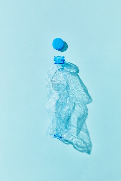 Bouteille vide en plastique utilisé sur un mur bleu pastel avec des ombres, place pour le texte. Concept pollution de l'environnement du plastique.