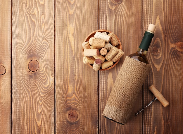 Bouteille de vin blanc, bol avec bouchons et tire-bouchon. Vue d'en haut sur fond de table en bois rustique