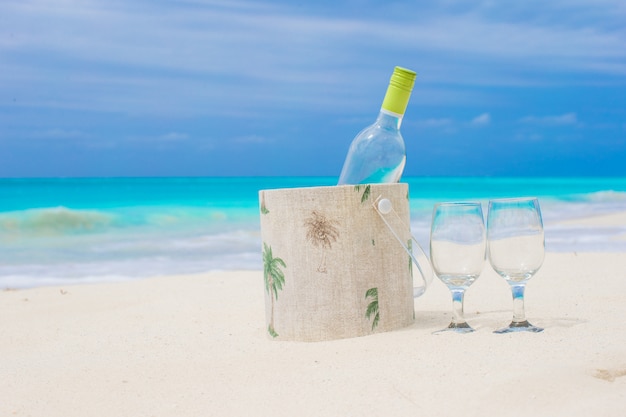 Bouteille de vin blanc et deux verres sur la plage de sable exotique