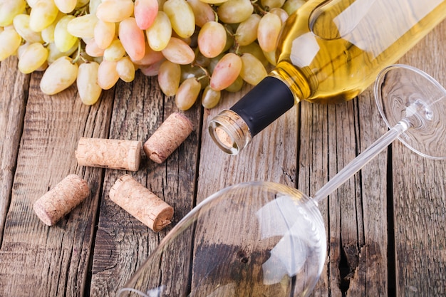 Bouteille de vin blanc, raisin et bouchons sur table en bois