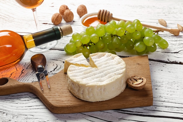 Photo bouteille de vin blanc, raisin, miel, fromage et verre à vin sur une planche en bois blanche