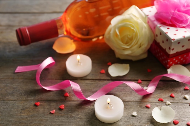 Une bouteille de vin, des bougies, une rose blanche et un cadeau dans la boîte, sur fond de bois