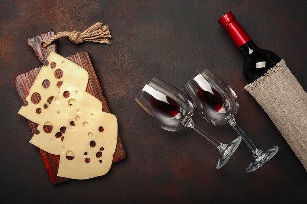 Bouteille de vin, deux verres et du fromage maasdam tranchés sur une planche à découper sur fond rouillé