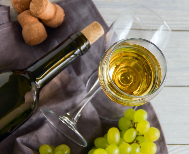 Bouteille de vin avec des raisins sur une table en bois blanche