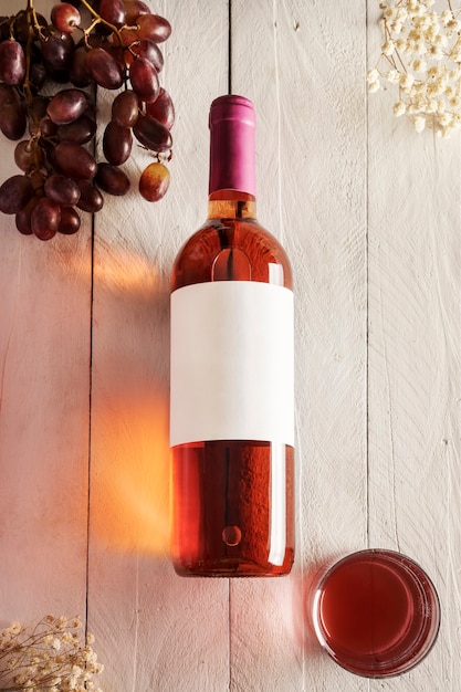 Bouteille de vin rosé avec une étiquette vierge et un verre de vin et de raisins