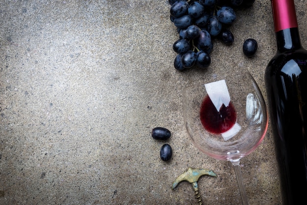 Une bouteille de vin rouge avec du verre et des raisins sur une pierre grise