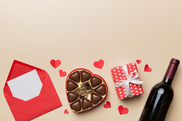 Bouteille de vin rouge sur fond coloré pour la Saint-Valentin avec boîte-cadeau, enveloppe et chocolat. En forme de coeur avec boîte-cadeau de chocolats vue de dessus avec espace de copie.