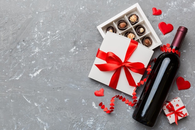 Bouteille de vin rouge sur fond coloré pour la Saint-Valentin avec cadeau et chocolat en forme de coeur avec boîte-cadeau de chocolats vue de dessus avec espace de copie