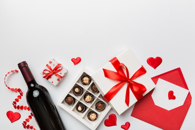 Bouteille de vin rouge sur fond coloré pour la Saint-Valentin avec enveloppe de boîte-cadeau et chocolat en forme de coeur avec boîte-cadeau de chocolats vue de dessus avec espace de copie