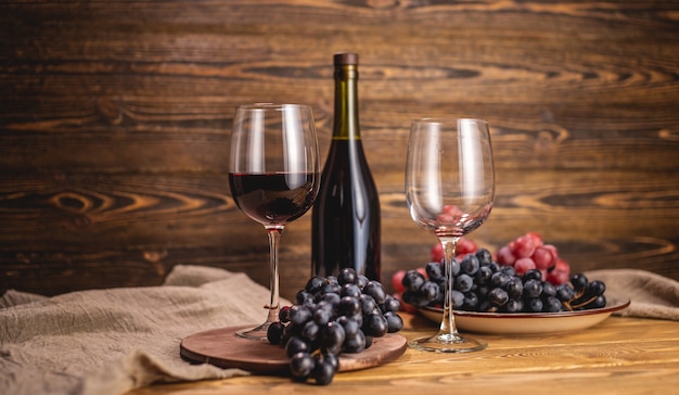 Une bouteille de vin rouge sec avec un verre et une grappe de raisin sur une table en bois