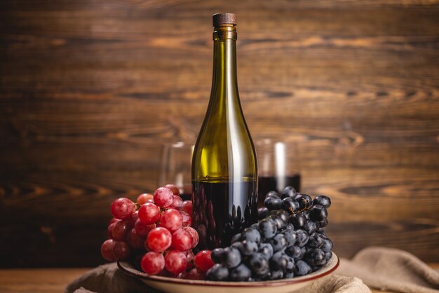 Une bouteille de vin rouge sec avec un verre et une grappe de raisin sur une table en bois