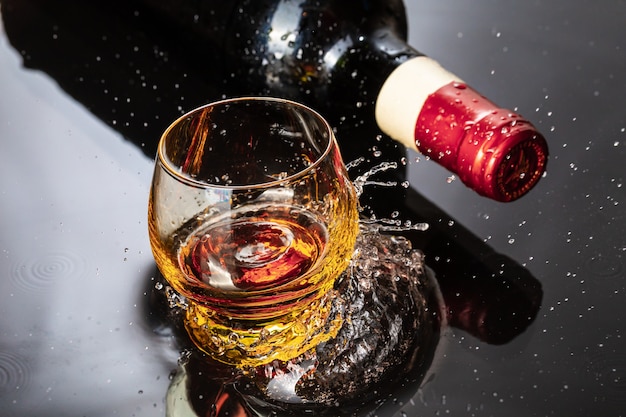 Bouteille de vin rouge avec verre à vin. Éclaboussure d'eau et gouttelette sur le reflet noir.