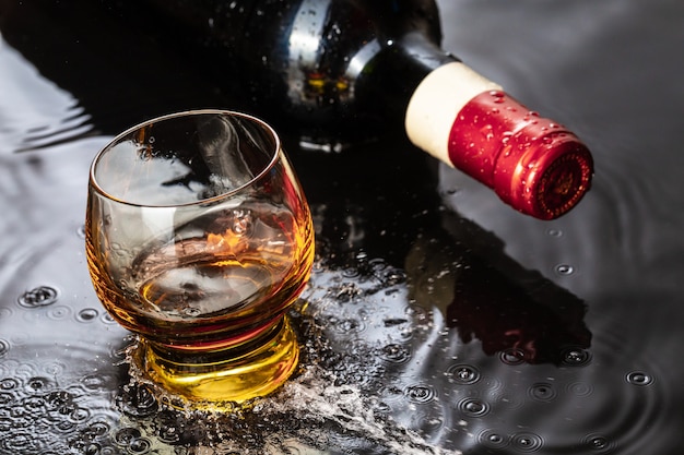 Bouteille de vin rouge avec verre à vin. Éclaboussure d'eau et gouttelette sur le reflet noir.