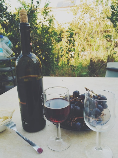 Photo une bouteille de vin rouge et un verre de vin et des raisins rouges sur la table.