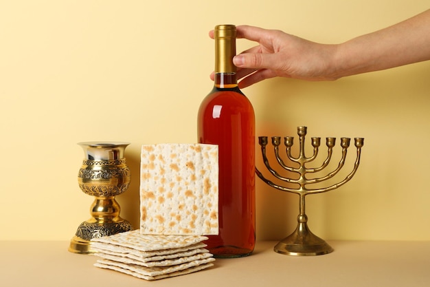 Bouteille de vin en tasse de matzo à la main et hanukkiah sur un fond jaune clair