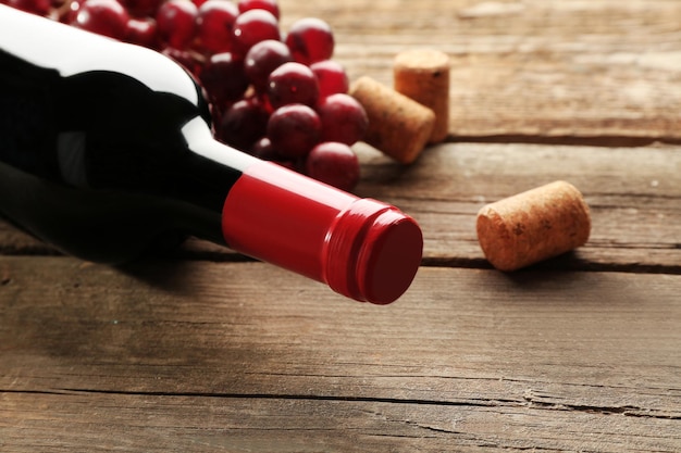 Bouteille de vin en verre avec bouchons et raisins sur fond de table en bois