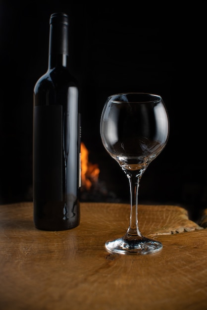 Bouteille de vin et verre vide sur une surface en bois rustique avec feu derrière