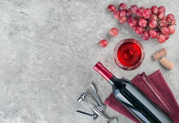 Bouteille de vin et verre à vin, grappe de raisin et tire-bouchon sur fond texturé gris. Vue de dessus, espace de copie.