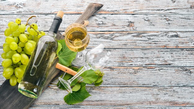 Une bouteille de vin avec des verres et des raisins Feuilles de raisin Vue de dessus Sur un fond en bois blanc Espace libre pour le texte