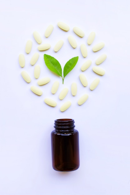 Bouteille de vitamine C et des pilules avec des feuilles vertes sur blanc