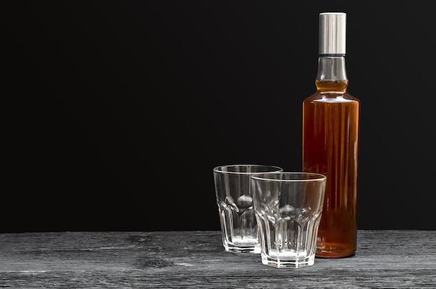 Bouteille de whisky avec deux verres vides sur fond noir Espace pour le texte