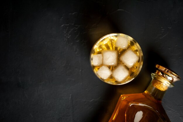 une bouteille de whisky et un verre de whisky avec de la glace sur du béton