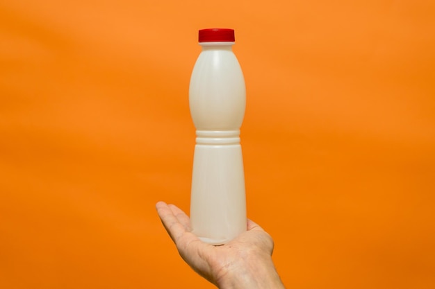 Bouteille de yaourt au lait dans la main de l'homme avec fond orange