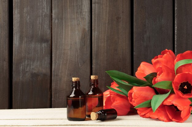 Bouteilles brunes en verre cosmétique et bouquet de tulipes rouges sur une table blanche contre un mur en bois sombre.